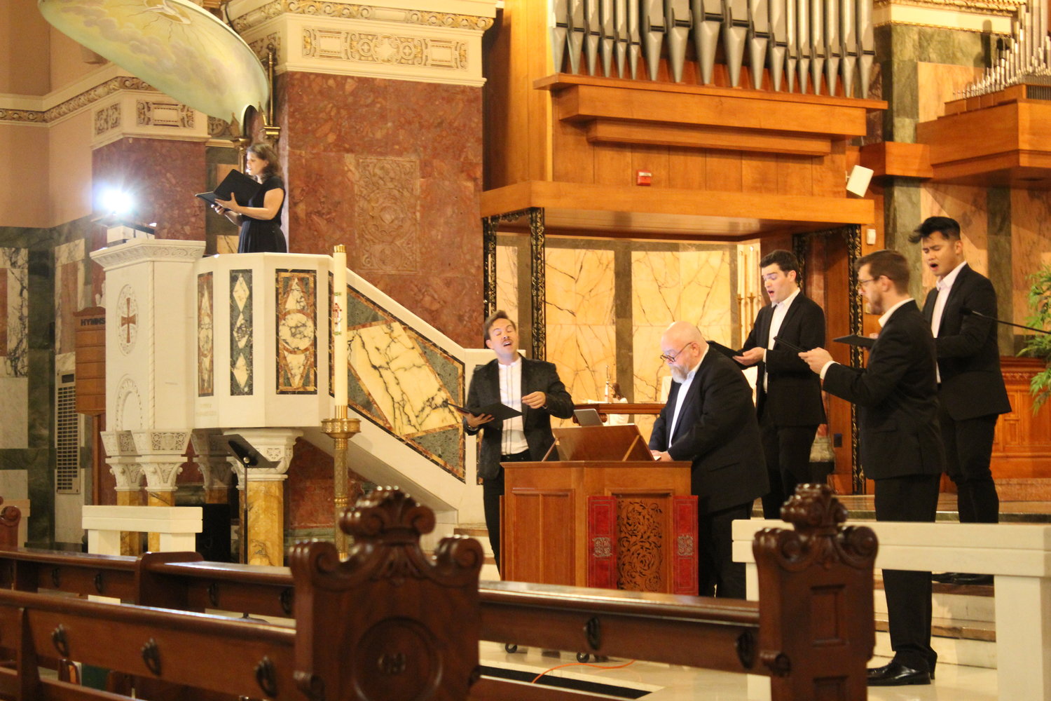 Members of Ensemble Altera perform at Blessed Sacrament Church in Providence. Our Lady of Mount Carmel Music Director Michael Garrepy and Ensemble Altera Director Christopher Lowrey appear third and fifth from the right, respectively; the choir director of the Church of St. Mary’s on Broadway, Rachel Garrepy, sings from the pulpit.